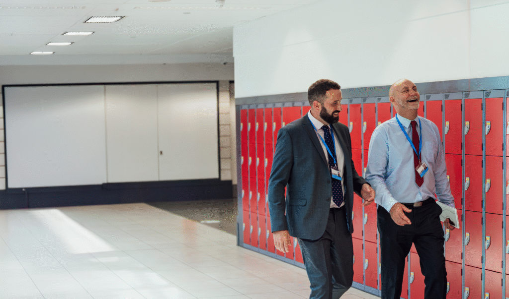 Two male teachers walking from class to another in high school where they work in New York. They are lauching as they walk and discuss leadership coaching for educators