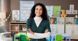 Woman, teacher with arms crossed smiling in classroom, proud of her educational leadership development and K-12 leadership training